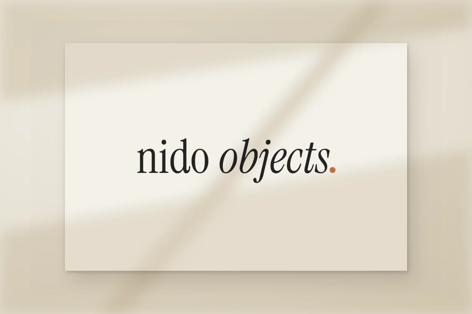 Nido Objects ordbild, ”nido objects.” med en orange punkt, tryckt på ett papperskort i mjukt fönsterljus.